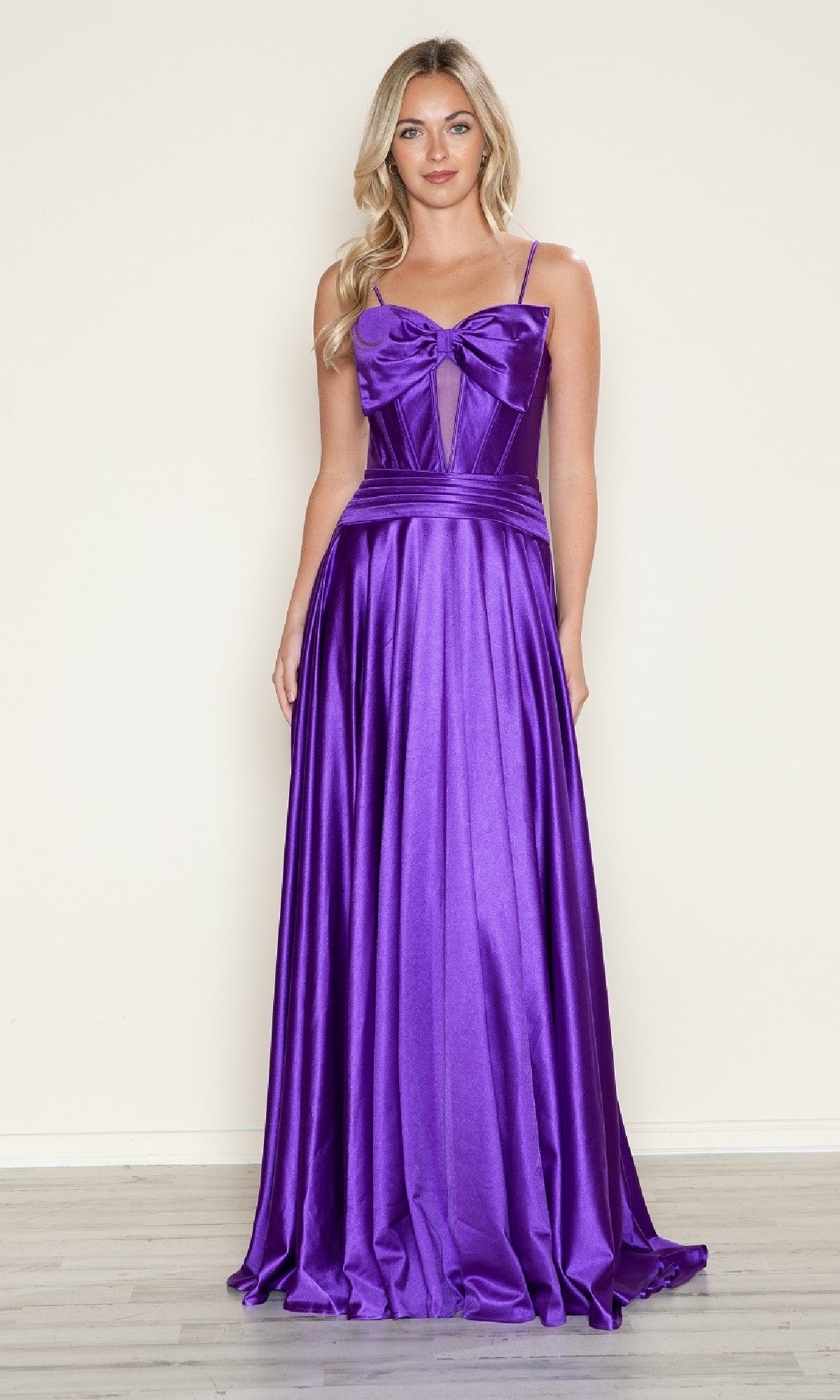 A woman wears the Bow-Front Long Corset Prom Dress (Poly USA 9702), a purple satin a-line gown with a large bow on the bodice, standing against a plain light-colored background.